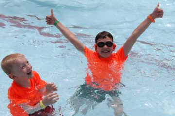 two boys having fun in a pool showing thumbs up