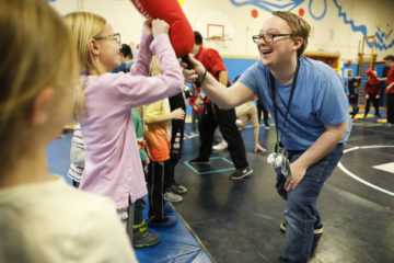 child in pink shirt blocking a martial arts pad from instructor in blue shirt smiling
