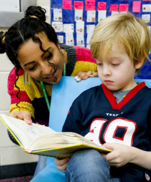 teacher looking over shoulder of boy reading a book